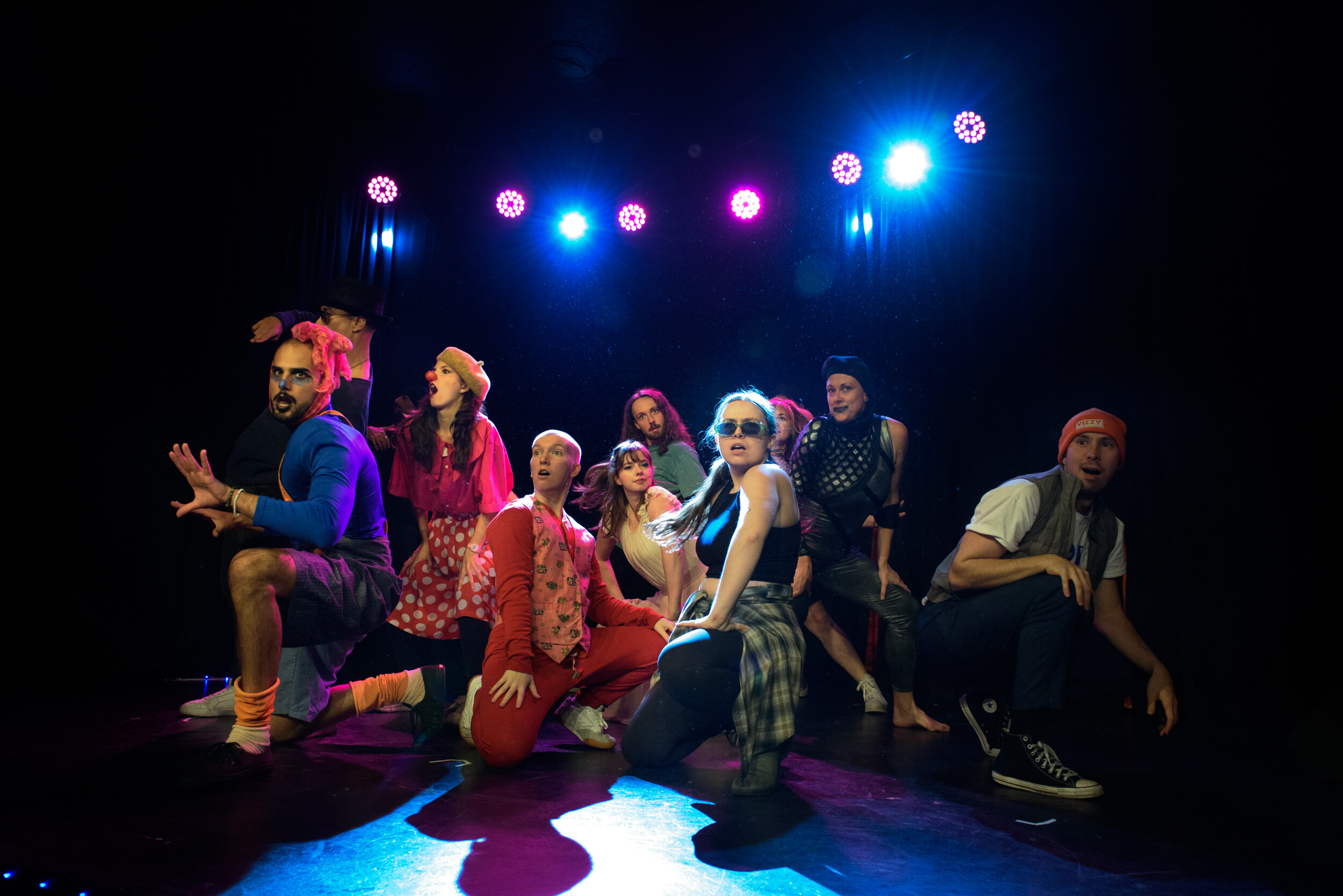 A group of performers are crouched on stage looking out to the audience.