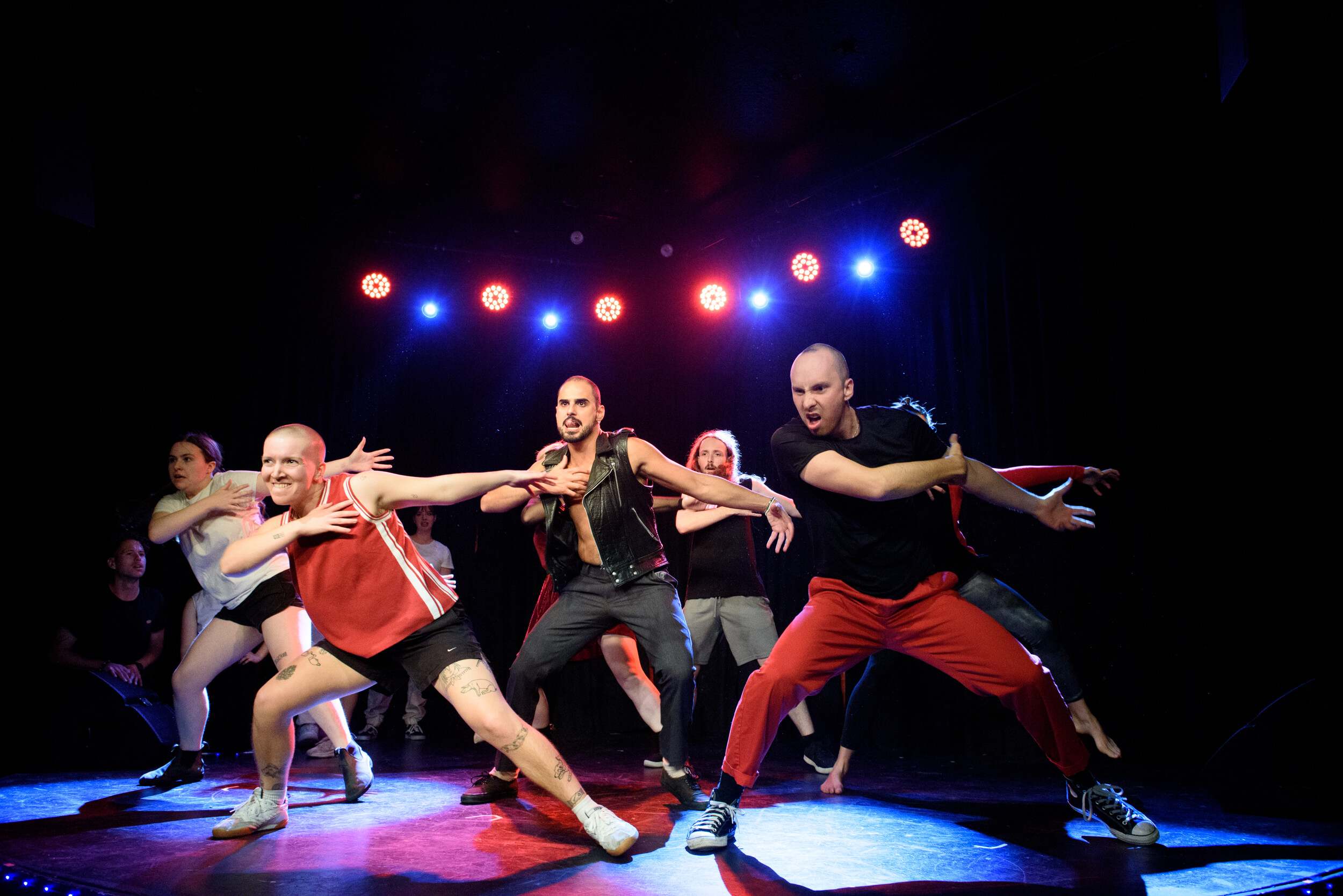 Performers are dancing. They are leaning to one side, holding their right arm across their chests with aggressive expressions on their faces.